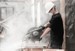 A worker in a hard hat and mask operates a circular saw to cut bricks, surrounded by dust in an active work environment.