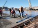 Site operative guiding a vibrating power screed beam across wet screed to achieve a level finish